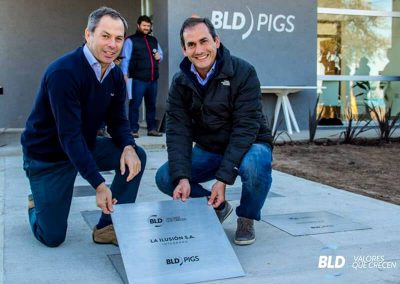Dos representantes de BLD Pigs colocando una placa cuadrada de acero inoxidable grabada en el piso