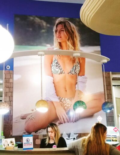 Cartel impreso en lona con la imagen de una modelo en bikini ubicada detrás de un mostrador de local comercial